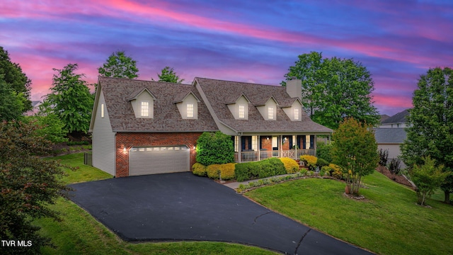 cape cod-style house with covered porch, asphalt driveway, brick siding, a chimney, and a yard