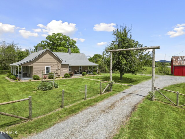 view of front facade with covered porch, a chimney, fence, a front yard, and gravel driveway