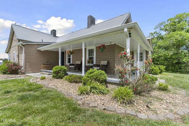rear view of property with a chimney, metal roof, a porch, and a lawn