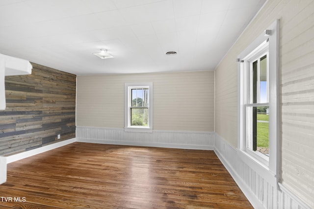 spare room with wood walls, visible vents, and wood finished floors