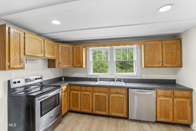 kitchen featuring dark countertops, light wood-style flooring, appliances with stainless steel finishes, and a sink