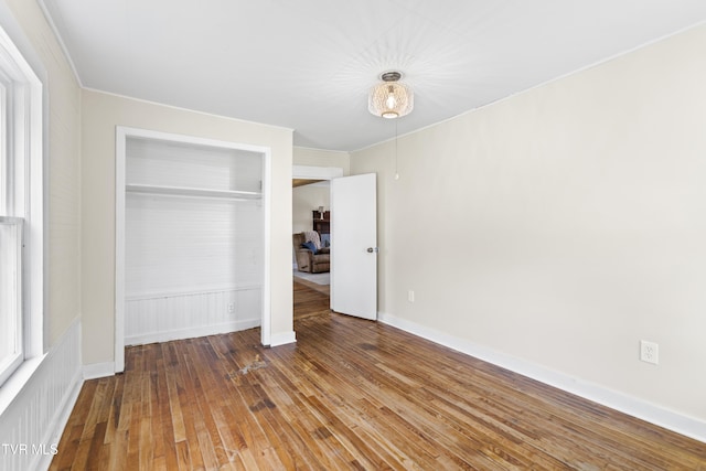 unfurnished bedroom featuring a closet, baseboards, wood-type flooring, and crown molding