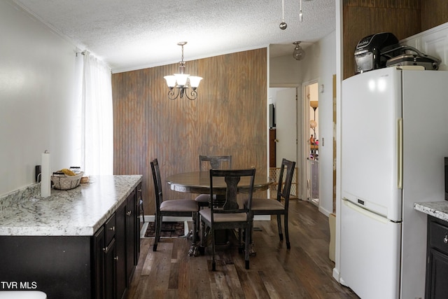 dining area featuring a notable chandelier, wood walls, dark wood finished floors, and a textured ceiling