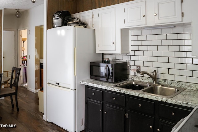 kitchen with freestanding refrigerator, dark cabinetry, a sink, stainless steel microwave, and white cabinets