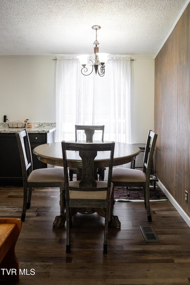 dining room featuring wood finished floors, a textured ceiling, visible vents, a chandelier, and wooden walls