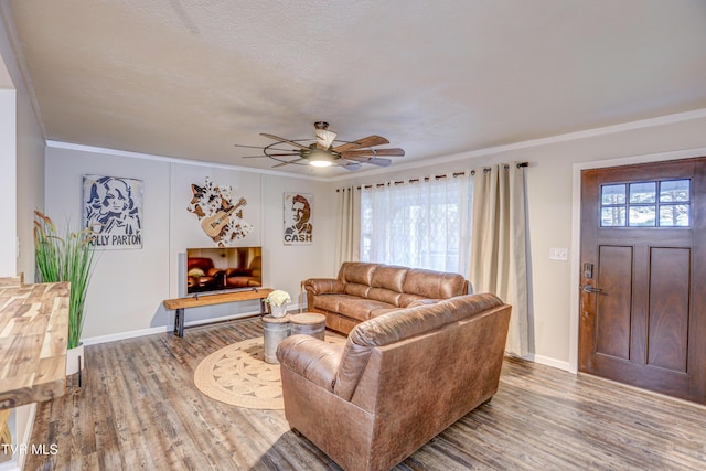 living area featuring baseboards, ornamental molding, a ceiling fan, and wood finished floors