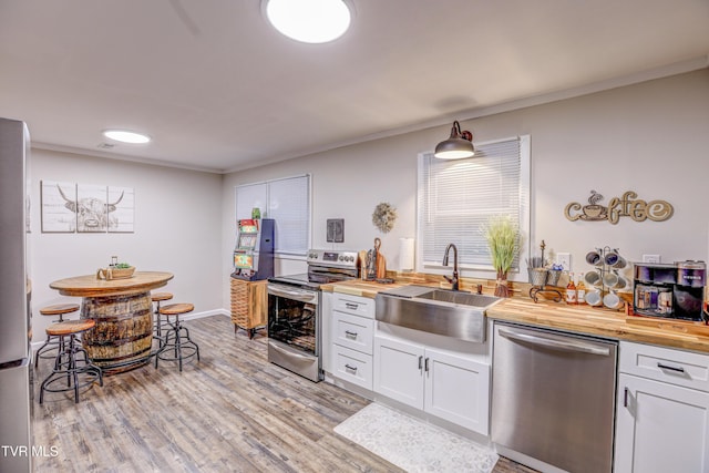 kitchen with a sink, butcher block counters, stainless steel appliances, and white cabinets