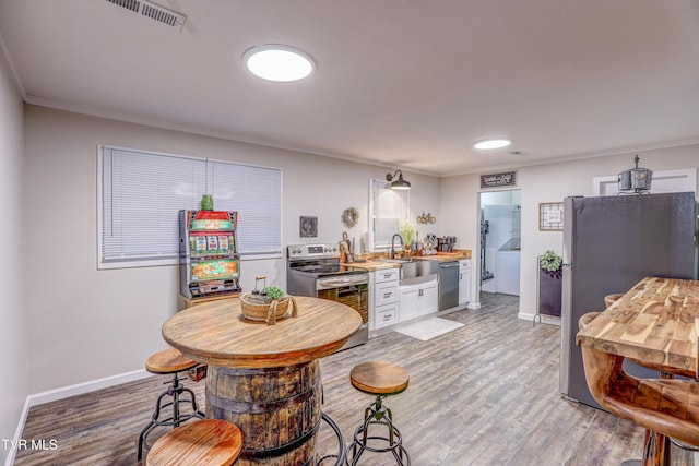 kitchen with a sink, visible vents, light wood-style flooring, white cabinetry, and appliances with stainless steel finishes