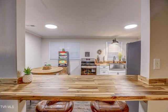 kitchen with wooden counters, stainless steel appliances, white cabinets, and a sink