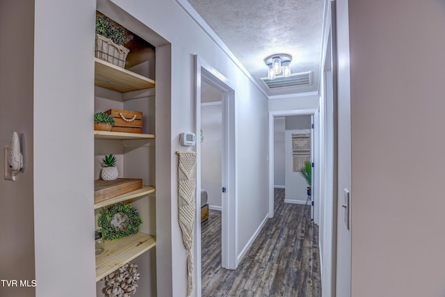 hallway featuring a textured ceiling, visible vents, dark wood-style flooring, crown molding, and baseboards