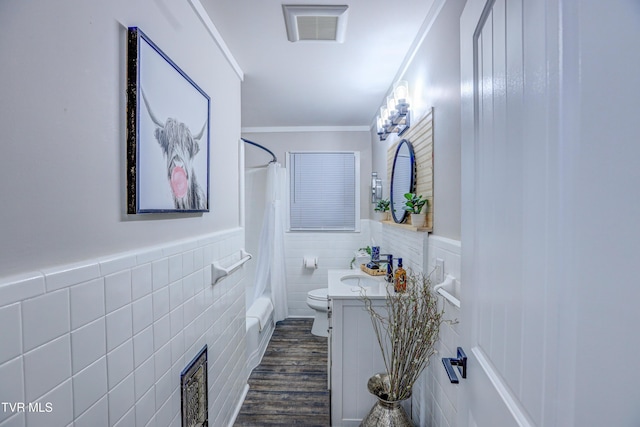 full bathroom featuring tile walls, toilet, visible vents, vanity, and a wainscoted wall