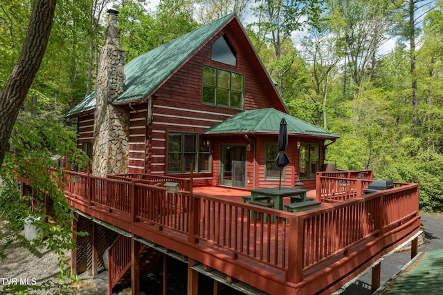 back of house featuring metal roof, a wooded view, a deck, and a chimney
