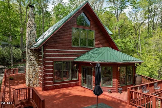 back of property featuring metal roof, a deck, log exterior, and a chimney