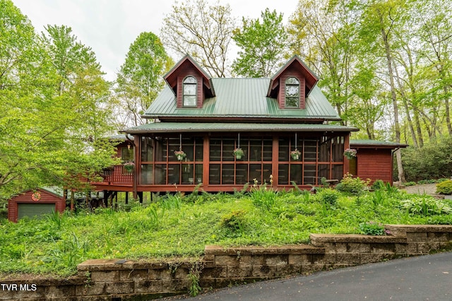 back of house featuring metal roof, a sunroom, a detached garage, and an outbuilding