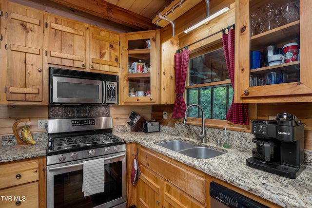 kitchen with a sink, light stone countertops, glass insert cabinets, and appliances with stainless steel finishes