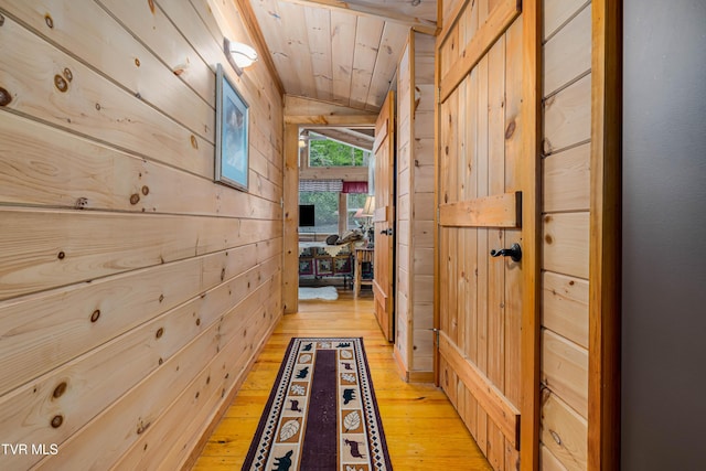 hall featuring vaulted ceiling, wooden ceiling, light wood-type flooring, and wooden walls