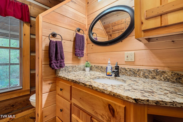 bathroom featuring toilet, wood walls, and vanity