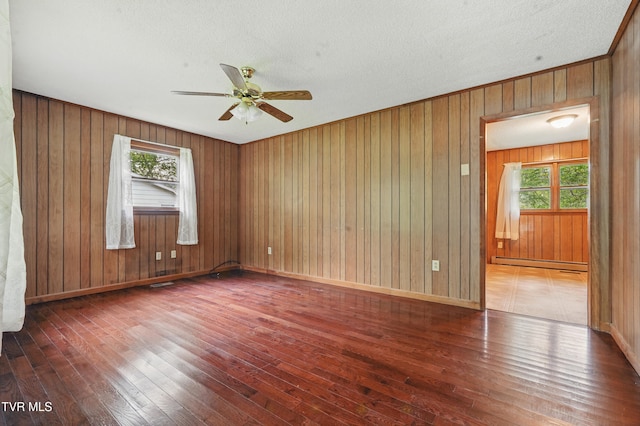 spare room featuring baseboard heating, a ceiling fan, a healthy amount of sunlight, and hardwood / wood-style flooring