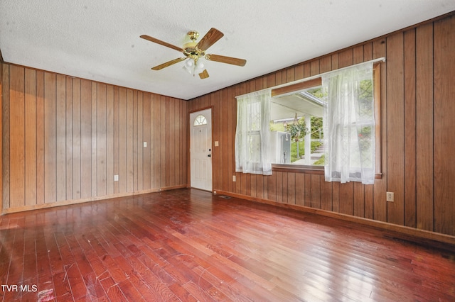 empty room with baseboards, wood walls, wood finished floors, and a ceiling fan