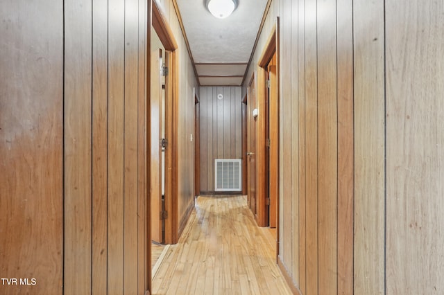 corridor with wood walls, light wood-type flooring, and visible vents
