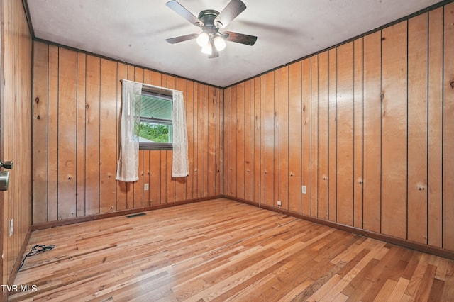 unfurnished room featuring a ceiling fan, baseboards, visible vents, wooden walls, and hardwood / wood-style flooring