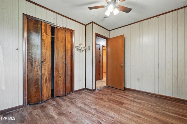 unfurnished bedroom with wood finished floors, a closet, baseboards, wooden walls, and ornamental molding