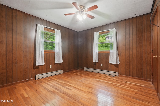 empty room with light wood-style floors, baseboard heating, and plenty of natural light