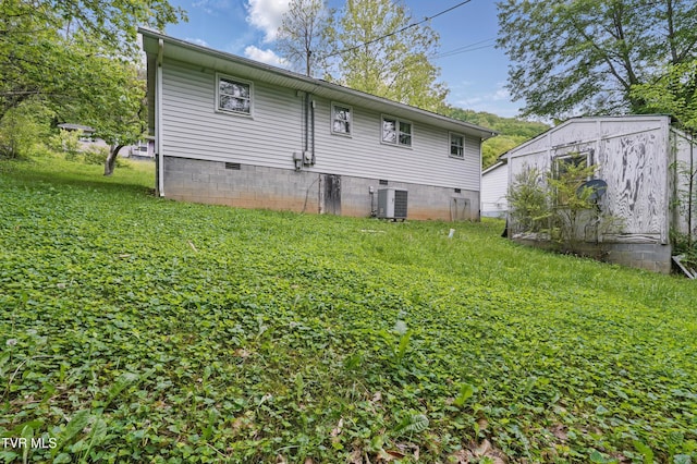 rear view of house with cooling unit, crawl space, and a lawn