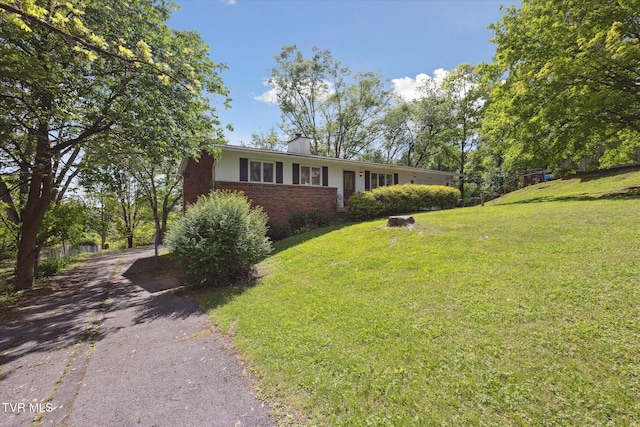 ranch-style house featuring brick siding, a front lawn, driveway, and a chimney