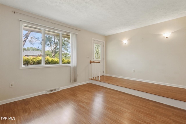 unfurnished room with plenty of natural light, wood finished floors, baseboards, and a textured ceiling