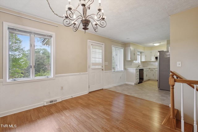 unfurnished dining area with a chandelier, a textured ceiling, light wood-style floors, baseboards, and wainscoting