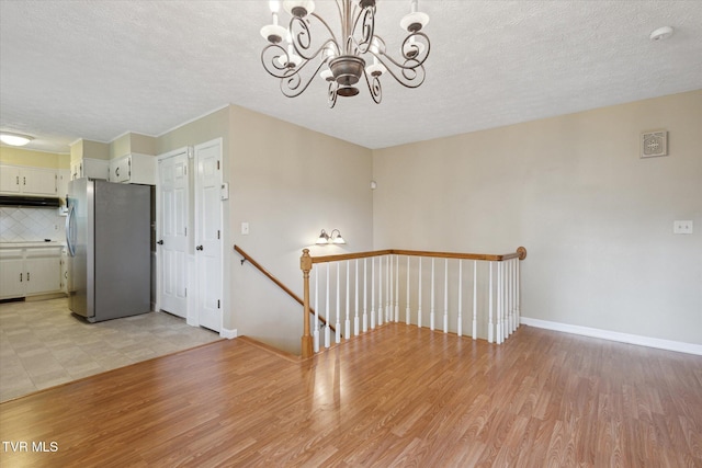 unfurnished room with a chandelier, light wood-style flooring, a textured ceiling, baseboards, and a smoke detector