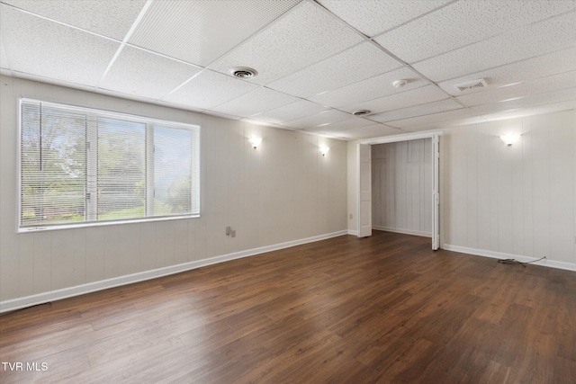 spare room with wood finished floors, a paneled ceiling, and baseboards
