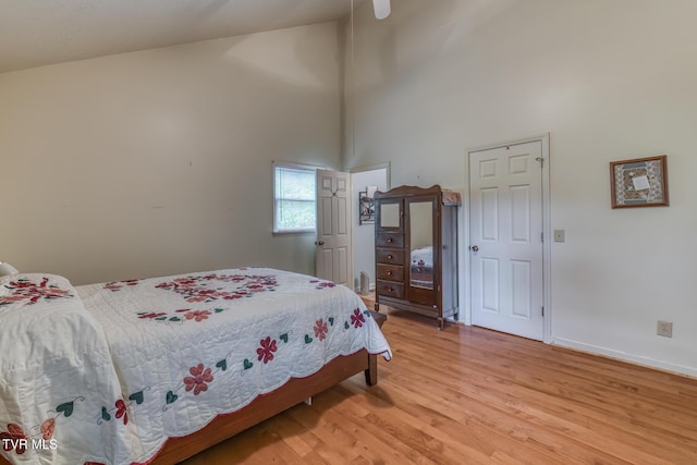 bedroom featuring baseboards, light wood-style flooring, and high vaulted ceiling