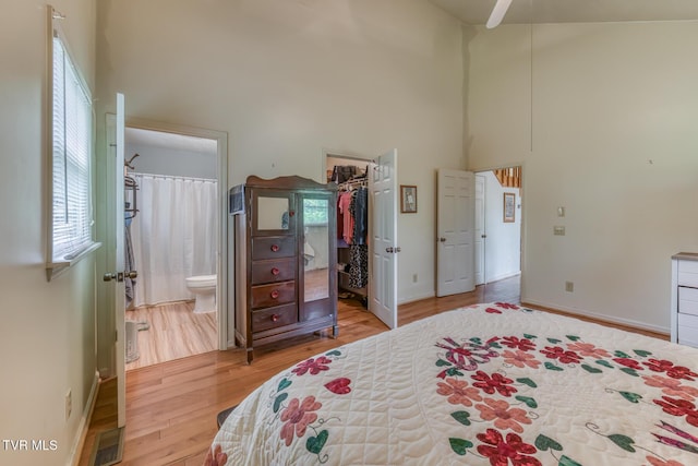 bedroom featuring a spacious closet, a high ceiling, ensuite bath, and wood finished floors