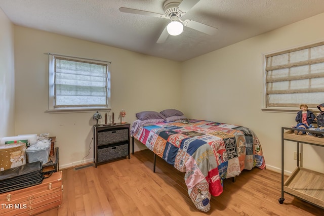 bedroom with ceiling fan, visible vents, a textured ceiling, and wood finished floors