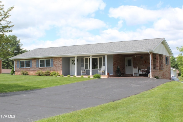 ranch-style house featuring brick siding, asphalt driveway, covered porch, a front lawn, and an attached carport