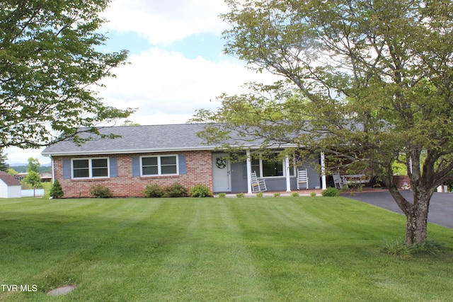 ranch-style house featuring a porch, brick siding, a front yard, roof with shingles, and asphalt driveway