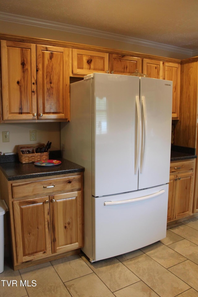 kitchen with freestanding refrigerator, dark countertops, ornamental molding, light tile patterned floors, and brown cabinetry