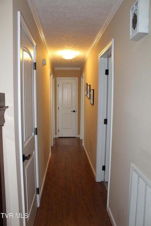 hall with wood finished floors, baseboards, a textured ceiling, and crown molding