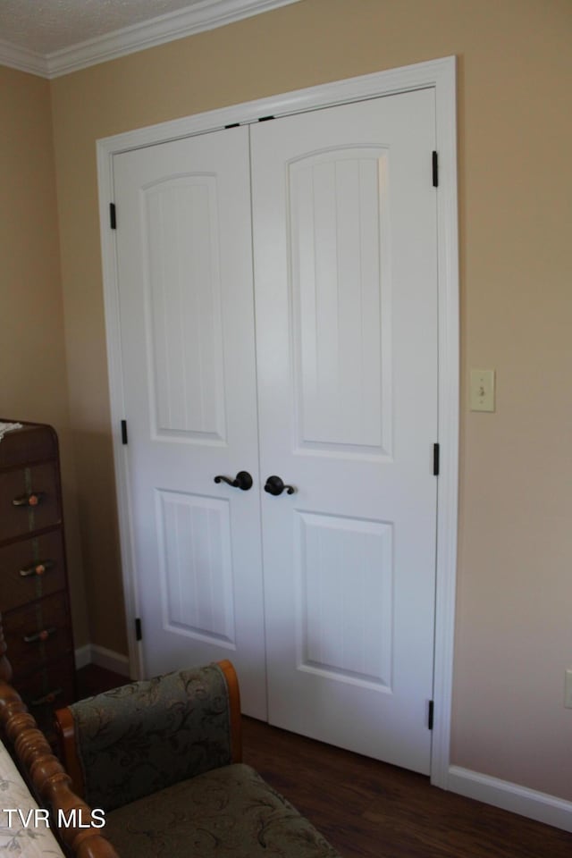 bedroom featuring wood finished floors, crown molding, a closet, and baseboards