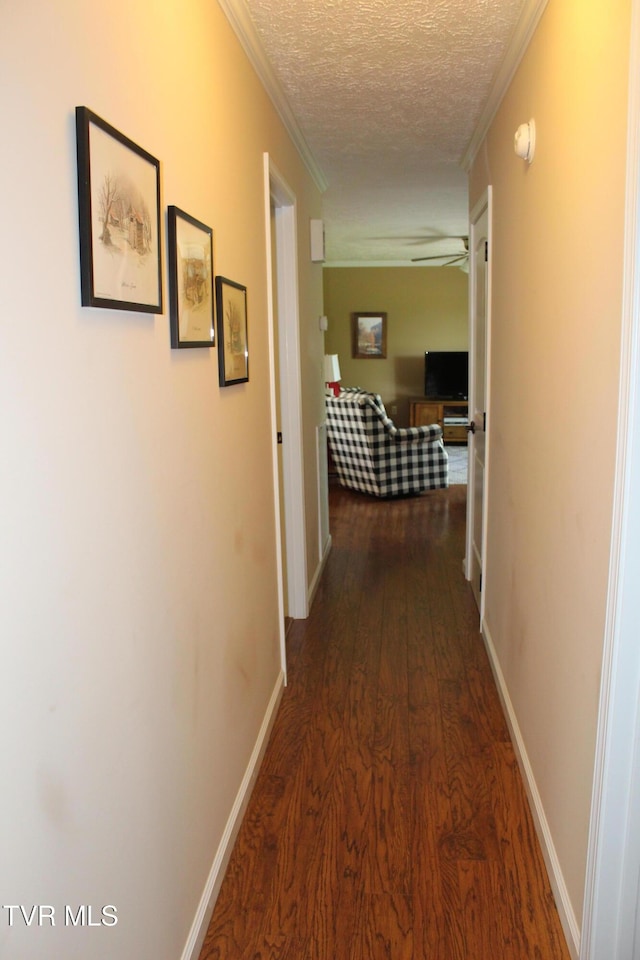 hallway featuring wood finished floors, a textured ceiling, baseboards, and ornamental molding
