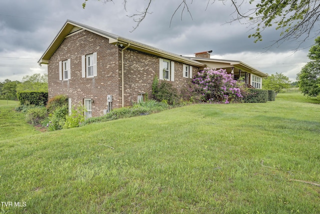 view of side of property with brick siding, a lawn, and a chimney