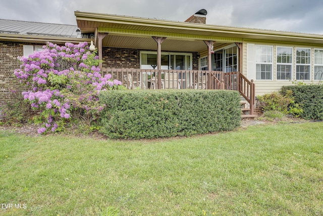 view of front of house with a porch, a front lawn, a chimney, and brick siding