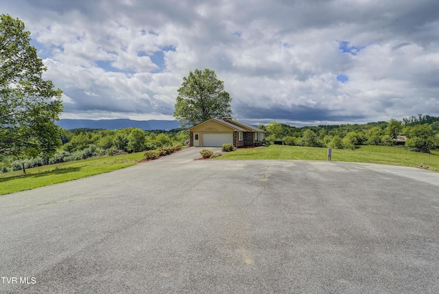 ranch-style home with asphalt driveway, an attached garage, a front yard, and a forest view