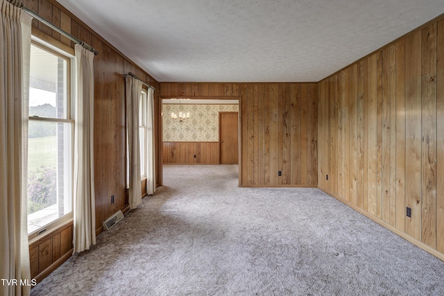 unfurnished room with a chandelier, a textured ceiling, carpet, and wood walls