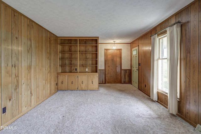 empty room with wooden walls, a textured ceiling, light carpet, and baseboards