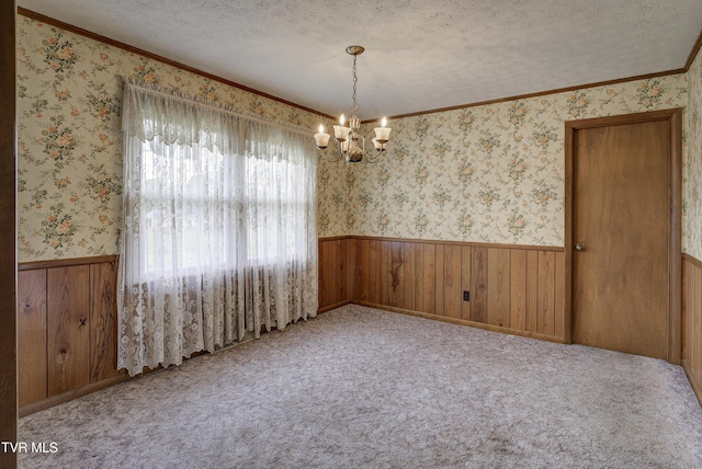 spare room with a wainscoted wall, a chandelier, a textured ceiling, crown molding, and wooden walls