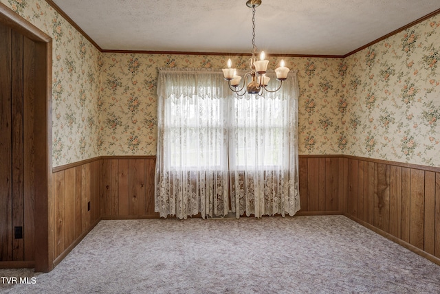 empty room with a chandelier, a textured ceiling, wainscoting, wooden walls, and crown molding