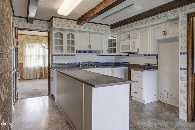 kitchen with wallpapered walls, white microwave, dark countertops, a sink, and glass insert cabinets